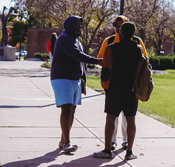 Three male students meeting on the campus sidewalk. The statue of Chief Little Turtle is in the background.