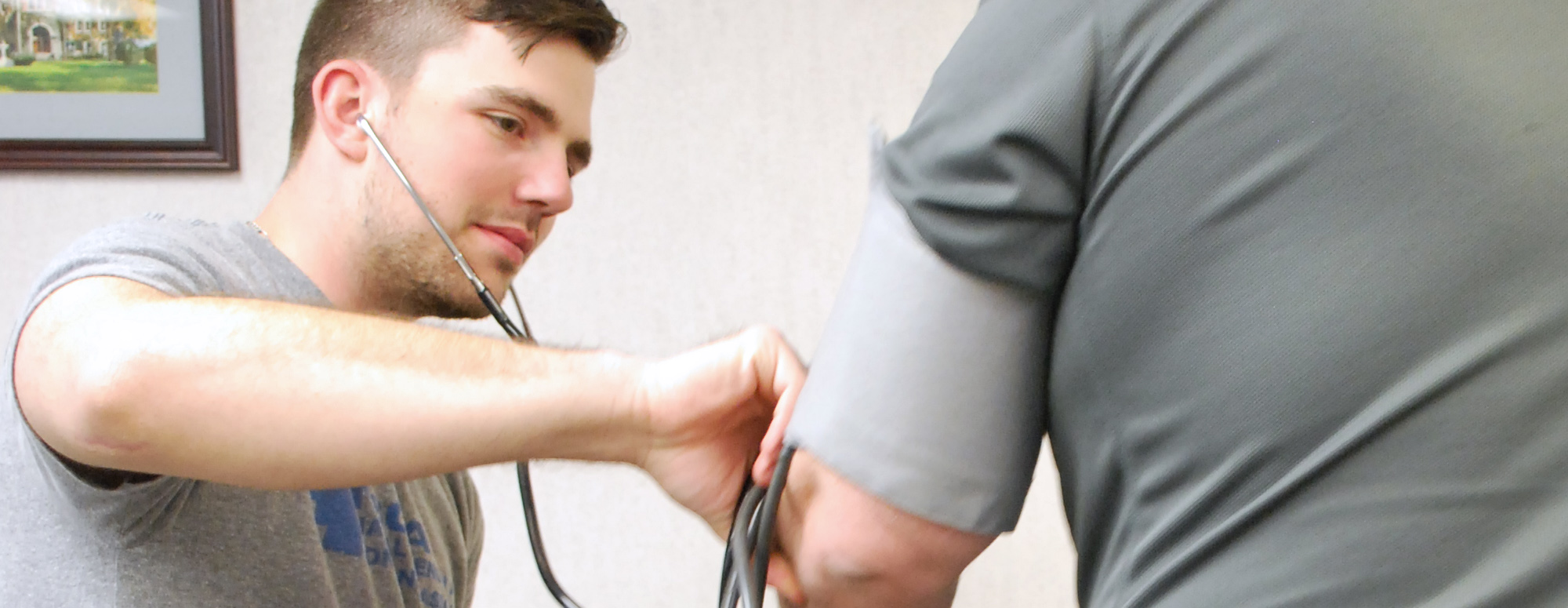 Male student with stethoscope working with an adult's arm