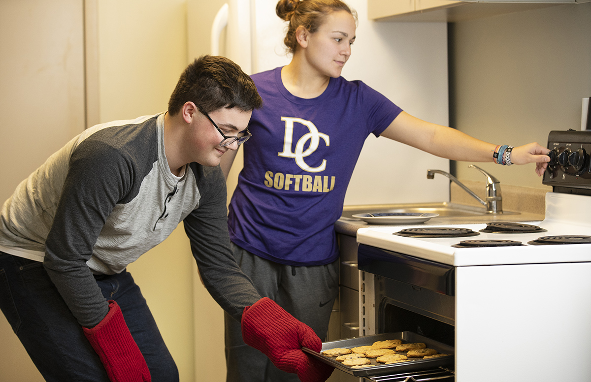 Male and female student standing by an oven to make cookies on a sheet