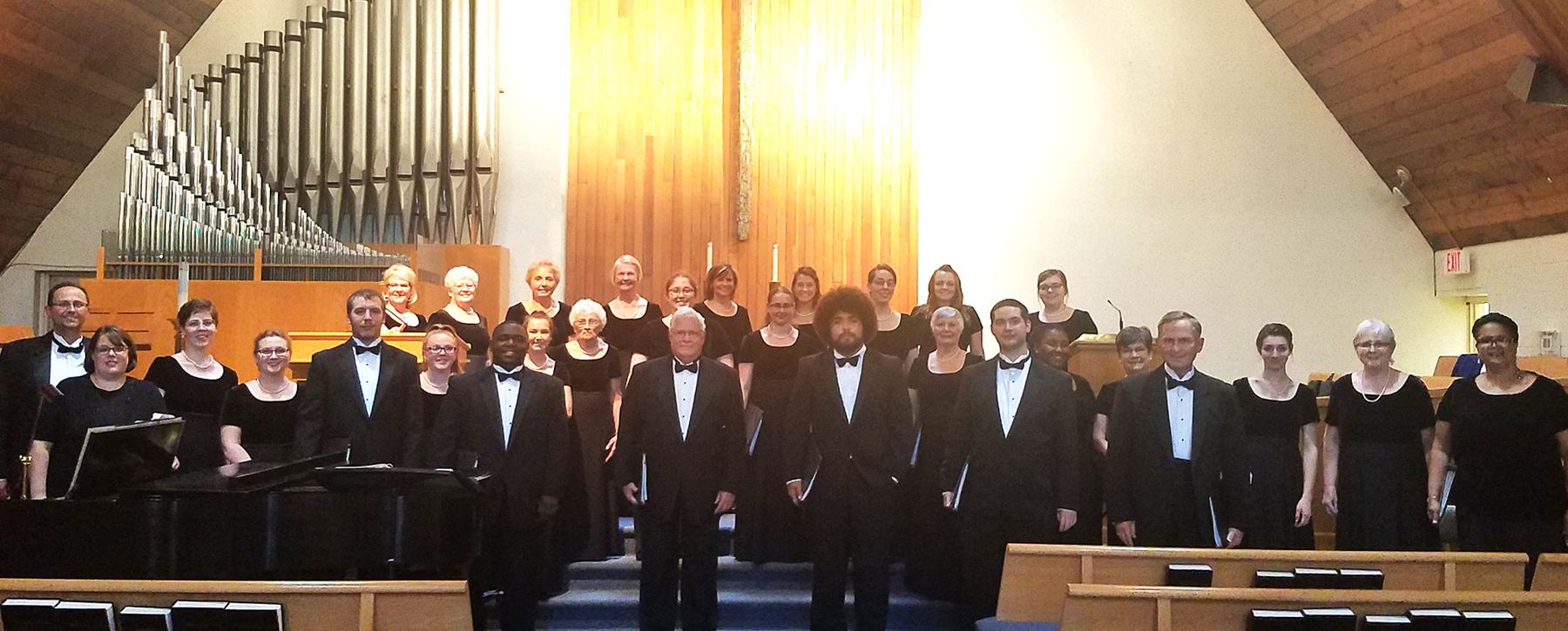 Thirty individuals standing together at the front of a church in black choir dress.