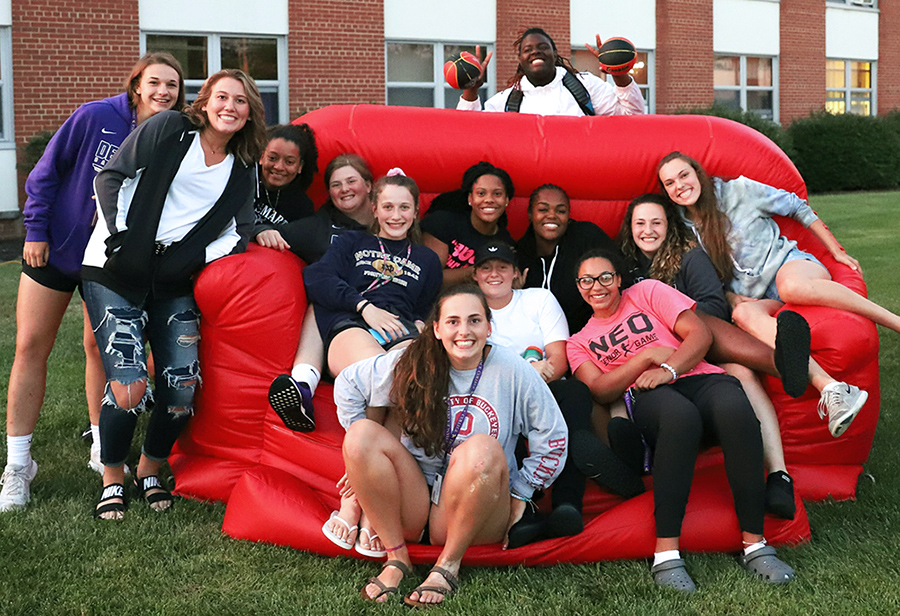 13 students gathered around a giant, red, inflatable chair and smiling at the camera