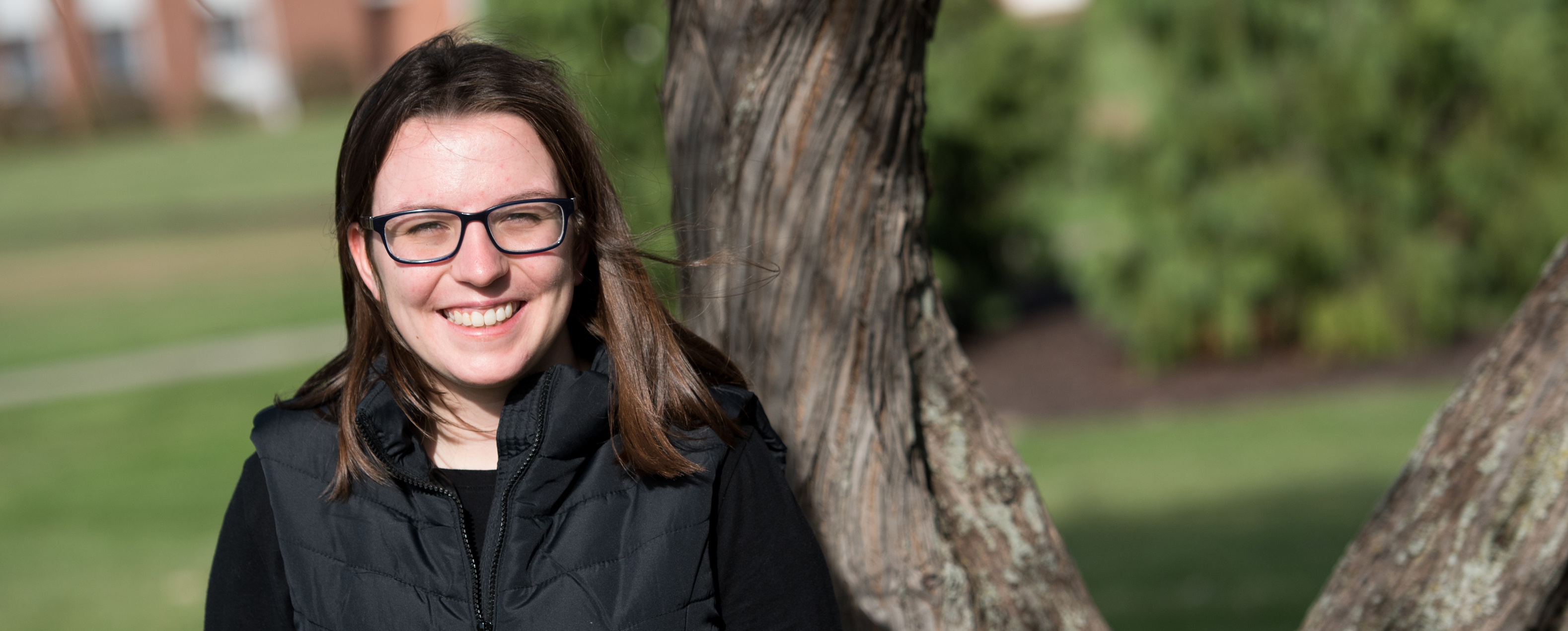 Female student with long, brown hair and glasses smiling at the camera